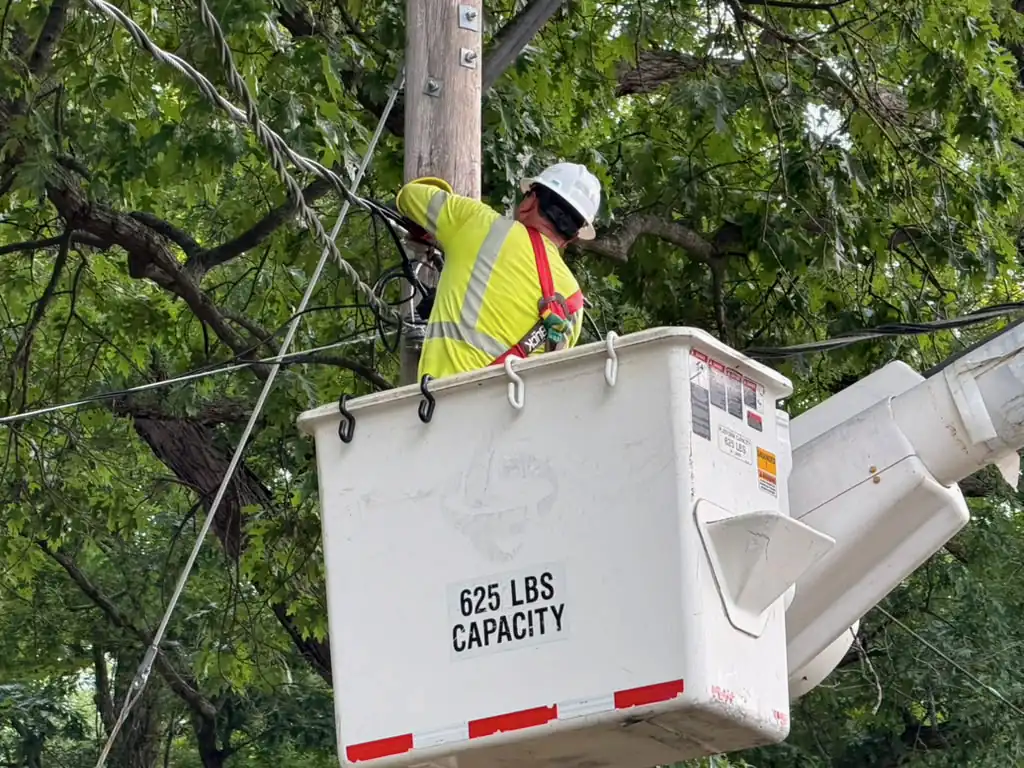 Lineman in a hard hat, hi-vis shirt and harness working from a bucket at a pole top